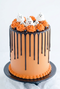 Halloween ghost drip cake with orange buttercream, dark chocolate ganache drips, white frosting ghosts, orange frosting swirls, and black Halloween sprinkles by The Makery Cake Co in Centennial, Colorado.