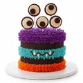 A Halloween-themed monster cake on a dark round platter, decorated with turquoise, brown, orange, and purple frosting stripes, a stitched smile, and five eye-shaped toppers on sticks by The Makery Cake Co in Denver.