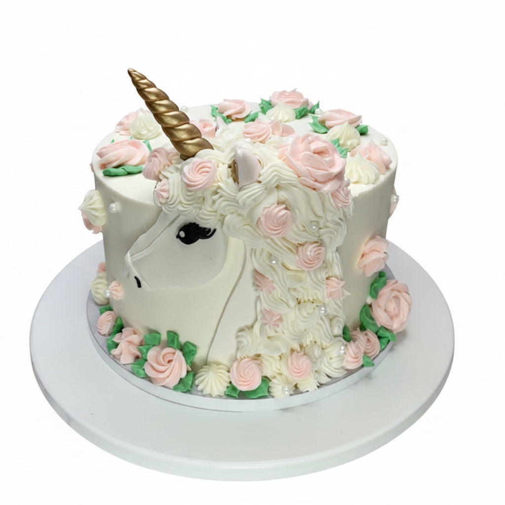 Unicorn-shaped cake with pink flowers and a gold horn on a white surface.