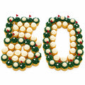 Two white platters decorated with cupcakes arranged to spell the number 50, each cupcake topped with white frosting and surrounded by green grass-like decorations with small red flags, set on a metal table.
