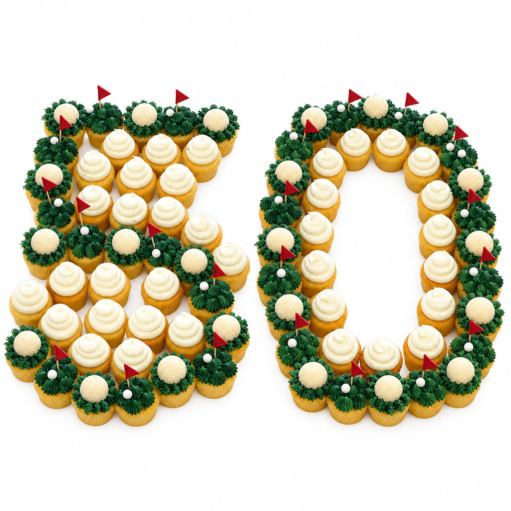 Two white platters decorated with cupcakes arranged to spell the number 50, each cupcake topped with white frosting and surrounded by green grass-like decorations with small red flags, set on a metal table.