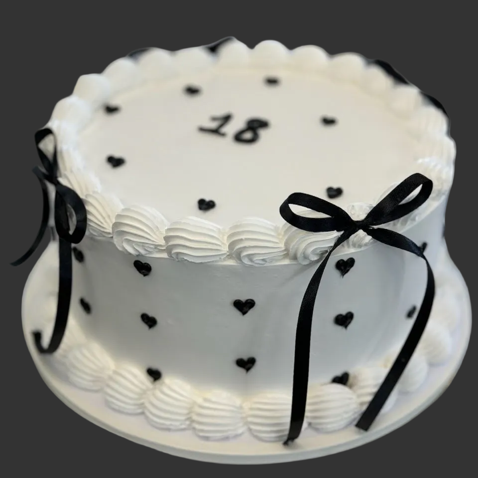 Two-layer white cake with black heart decorations and a number on top.